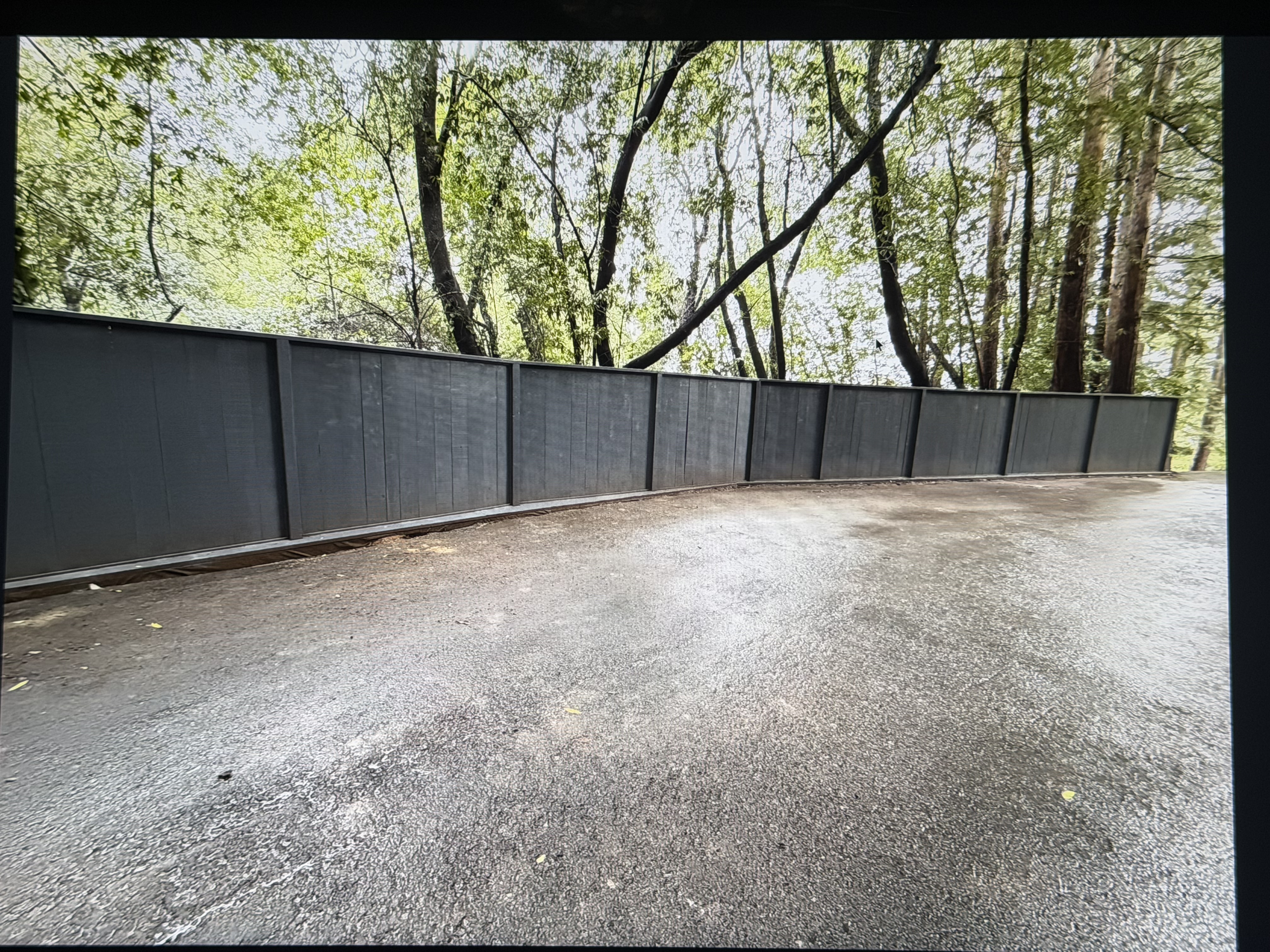 Custom dark fence installation by Mestow Landscaping in a wooded driveway